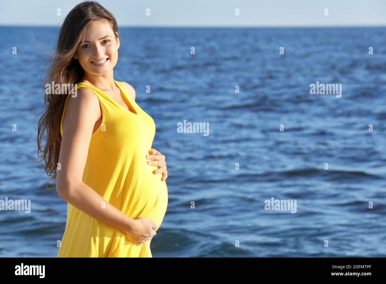 Jeune femme enceinte en robe jaune debout sur la plage Photo Stock - Alamy