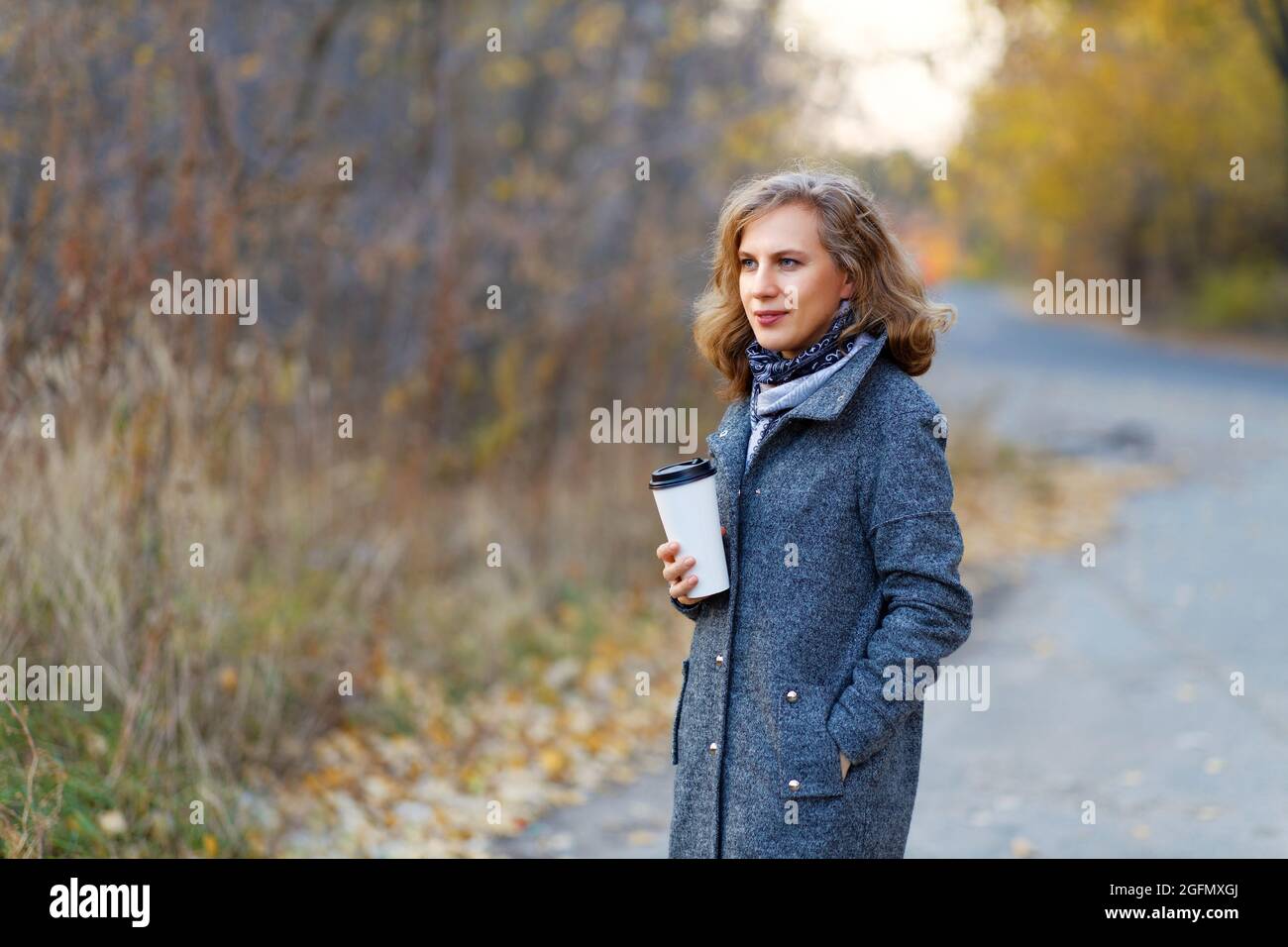 Portrait d'une jeune femme avec une tasse de carton de café sur le fond de la route et de la forêt d'automne. Mise au point Sahllow et arrière-plan flou. Banque D'Images Portrait d'une jeune femme avec une tasse de carton de café sur le fond de la route et de la forêt d'automne. Mise au point Sahllow et arrière-plan flou. Banque D'Images