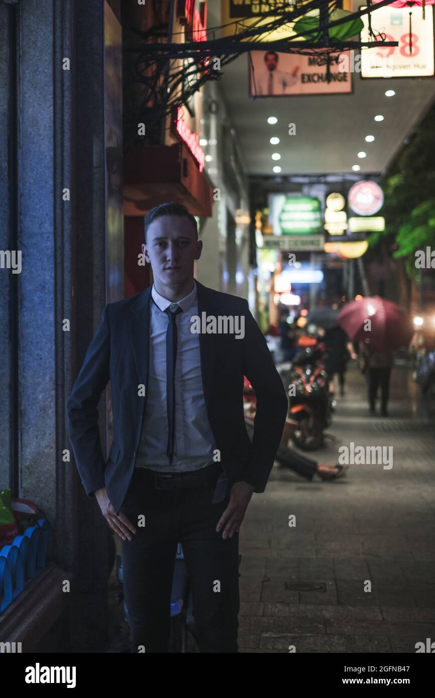 Portrait d'un jeune homme d'affaires élégant et riche en costume élégant se dresse dans la rue avec des lumières dans la grande ville. Image de nuit. Enseignes au néon Banque D'Images