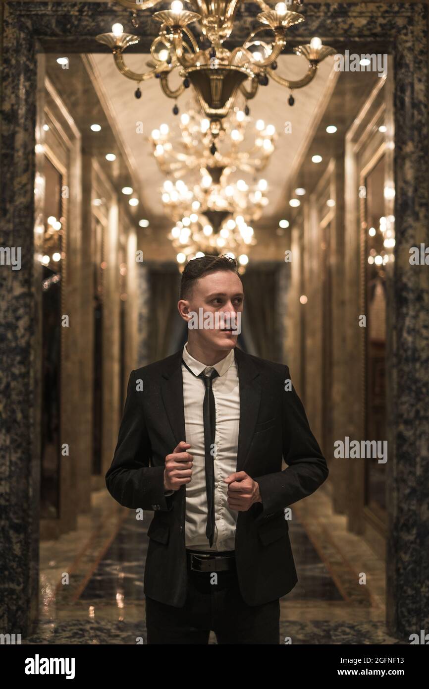 Portrait d'un jeune homme d'affaires beau dans un élégant costume d'affaires marchant dans le hall avec de beaux lustres chers. Tenant sa veste Banque D'Images