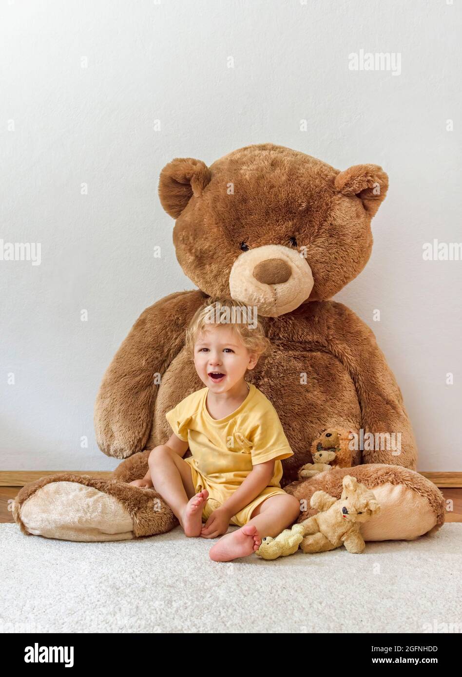 Un enfant adorable et heureux jouant avec son ours en peluche géant, à l'intérieur à la maison Banque D'Images