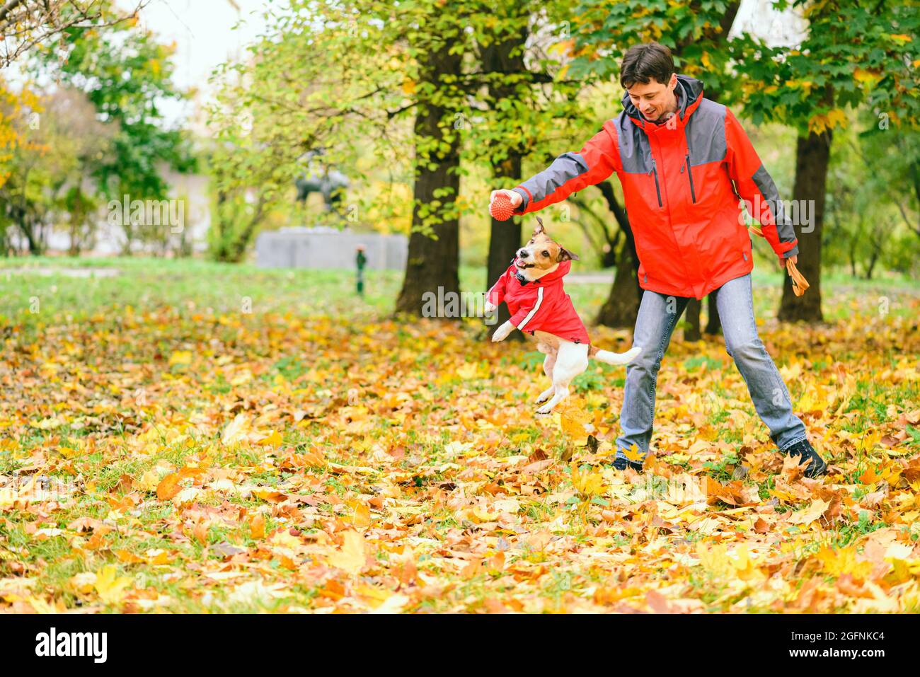 Homme et chien portant des manteaux similaires rouges jouant ensemble et s'amusant dans le parc d'automne Banque D'Images