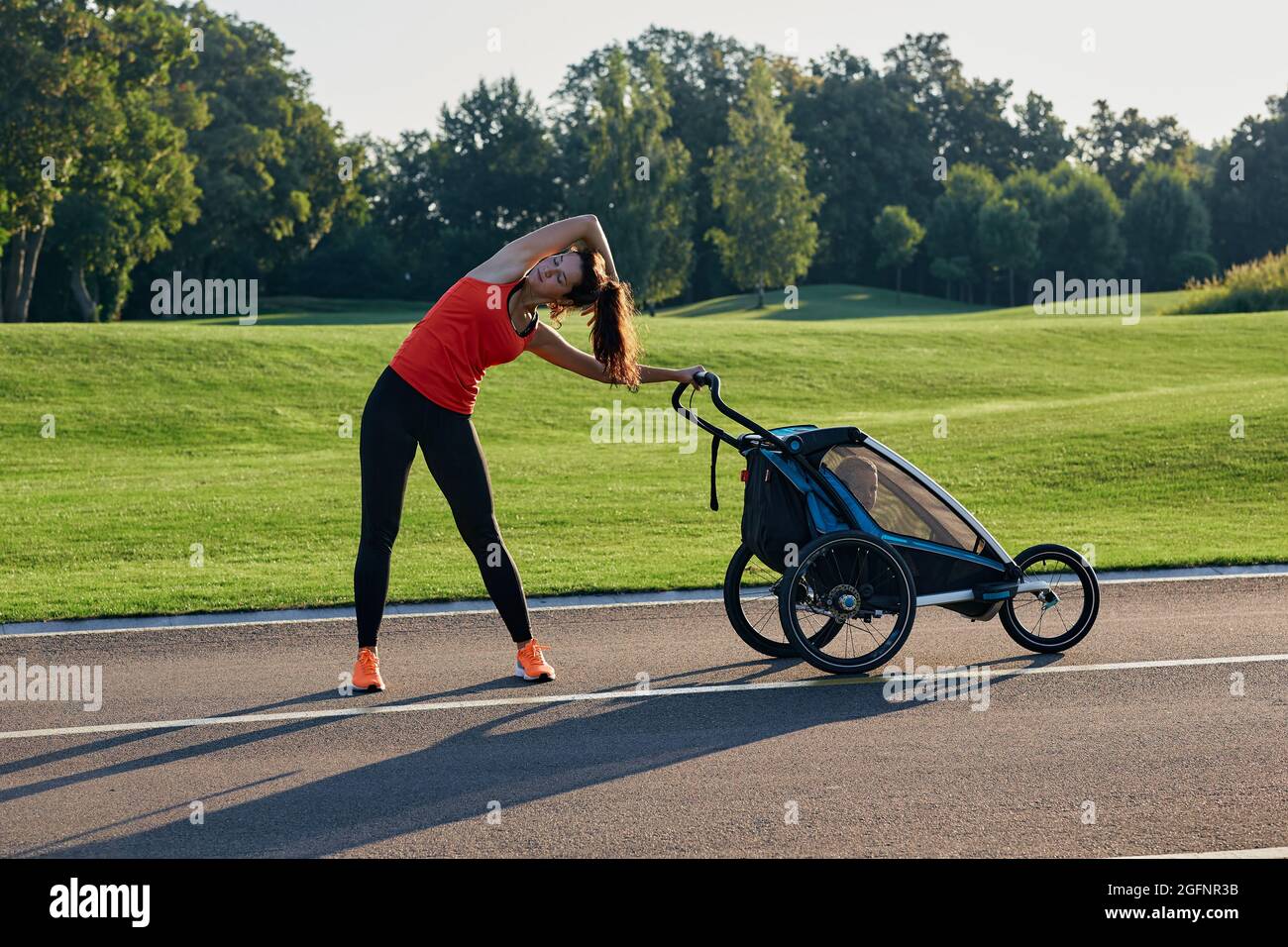 Jeune femme faisant de la gymnastique tout en marchant avec son enfant dans la poussette de bébé au parc public. Partie d'un ensemble d'exercices pour les jeunes femmes avec des enfants du Banque D'Images