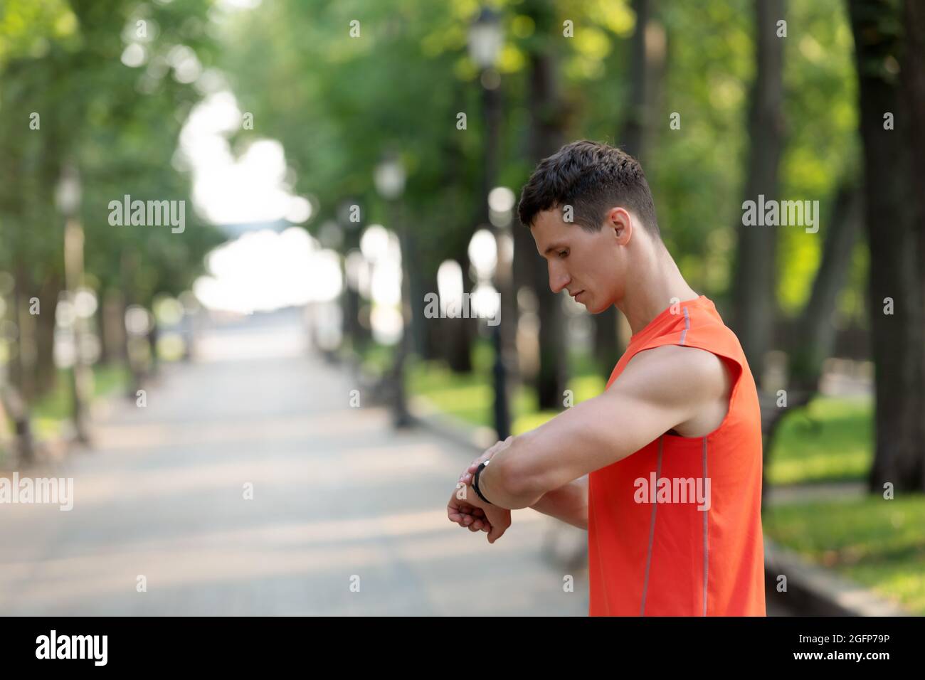 Un sportif vérifie le temps sur la montre-bracelet pendant l'entraînement sportif en plein air dans le parc, le calendrier sportif Banque D'Images