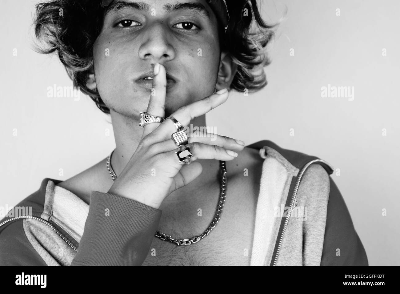 Photo en niveaux de gris d'un type indien frais portant un bandana et des anneaux tenant un doigt sur les lèvres Banque D'Images