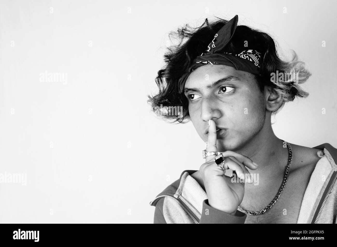 Photo en niveaux de gris d'un type indien frais portant un bandana et des anneaux tenant un doigt sur les lèvres Banque D'Images