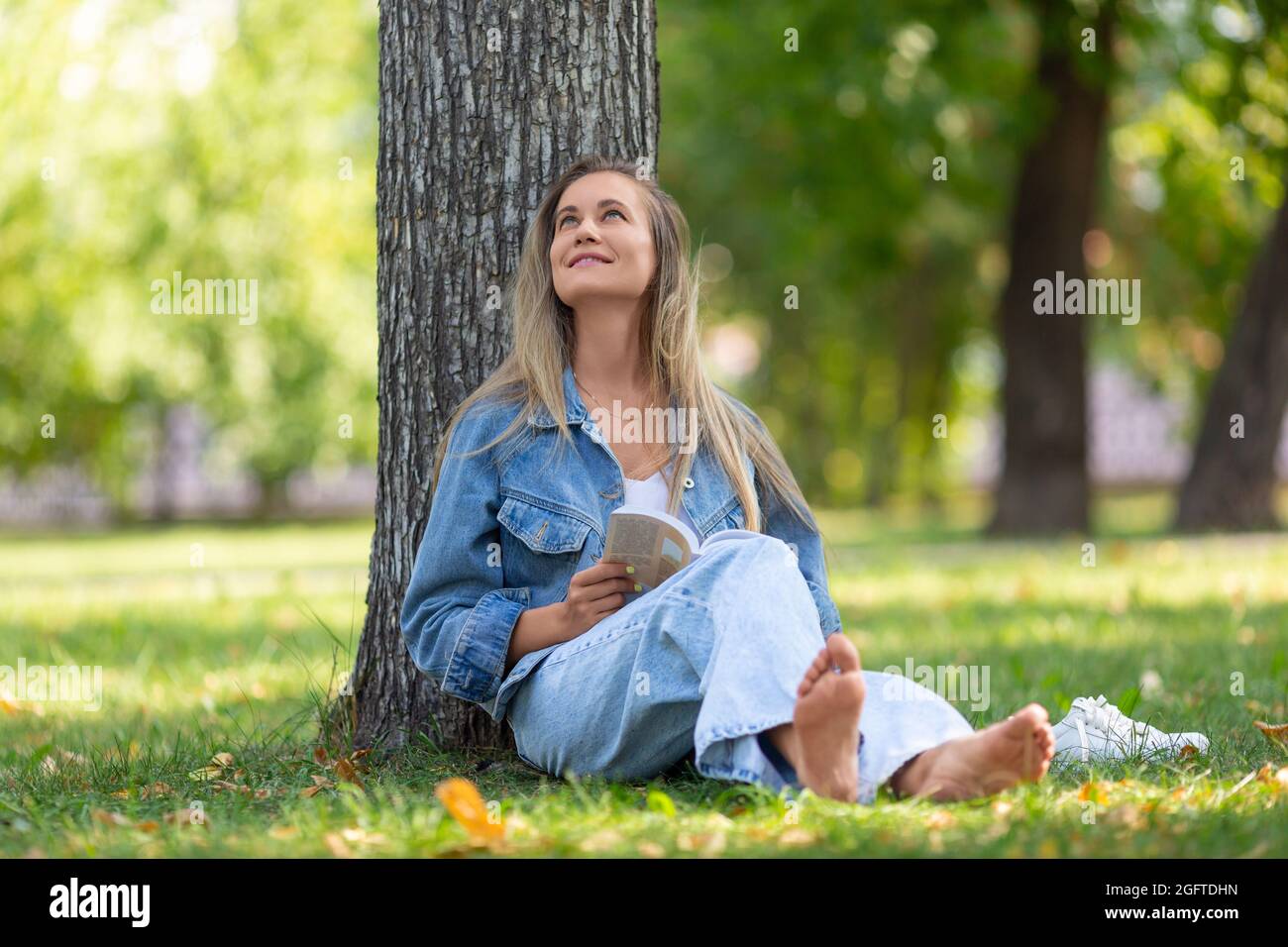 Bonne femme riant avec un livre sous l'arbre dans le parc de la ville. Concept de repos des gadgets et de l'agitation de la ville. Banque D'Images