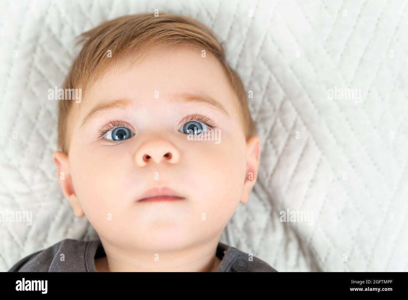 Portrait en gros plan d'un bébé de neuf mois. Bleu yeux rouge chevreau allongé sur le lit regardant l'appareil photo Banque D'Images
