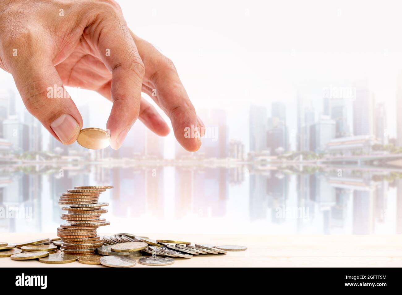 Main humaine plaçant une pièce de monnaie sur un tas de pièces avec un fond de gratte-ciel flou, utilisation pour les concepts d'affaires et de croissance financière. Banque D'Images Main humaine plaçant une pièce de monnaie sur un tas de pièces avec un fond de gratte-ciel flou, utilisation pour les concepts d'affaires et de croissance financière. Banque D'Images