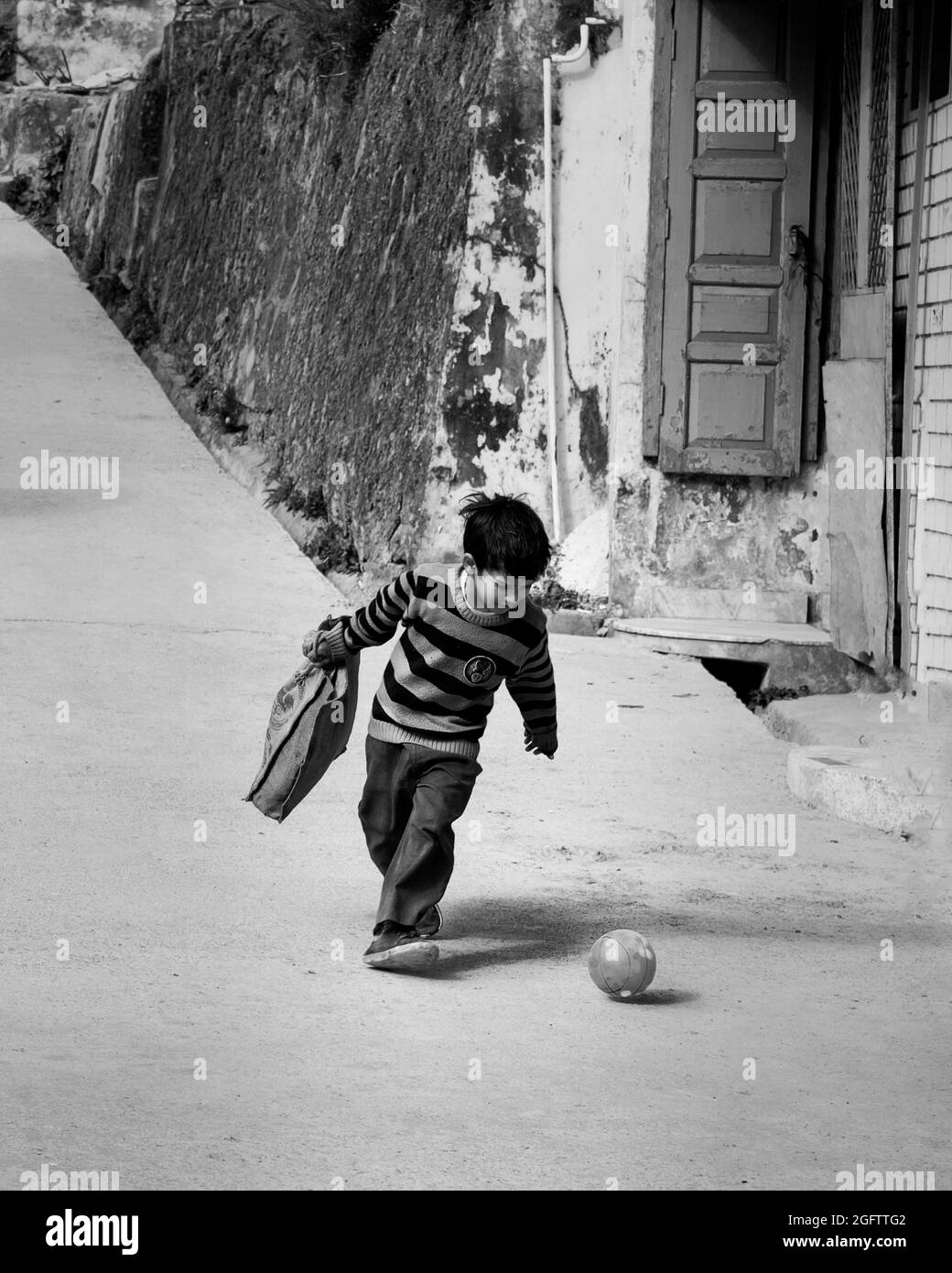 Photographie de rue en noir et blanc d'un jeune enfant jouant au football dans les rues seulement Banque D'Images