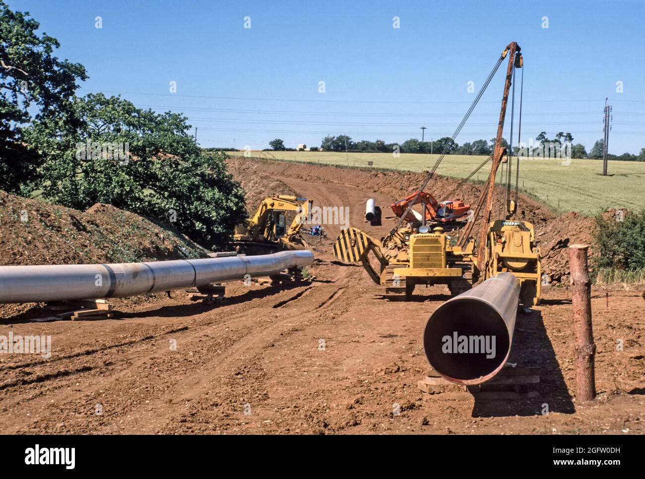 Vue d'archives des cultures dans les terres agricoles ouvertes en 1990 paysage rural marqué par les années 1990 lourd déplacement de la terre en génie civil équipement excavant une tranchée profonde pour de nouveaux tuyaux principaux de gaz d'acier de grand diamètre dans un nouveau pipeline de fond dans les années 90 Image d'archive de jour ciel bleu ensoleillé partie de la tiret britannique pour le gaz dans l'Essex Angleterre Banque D'Images