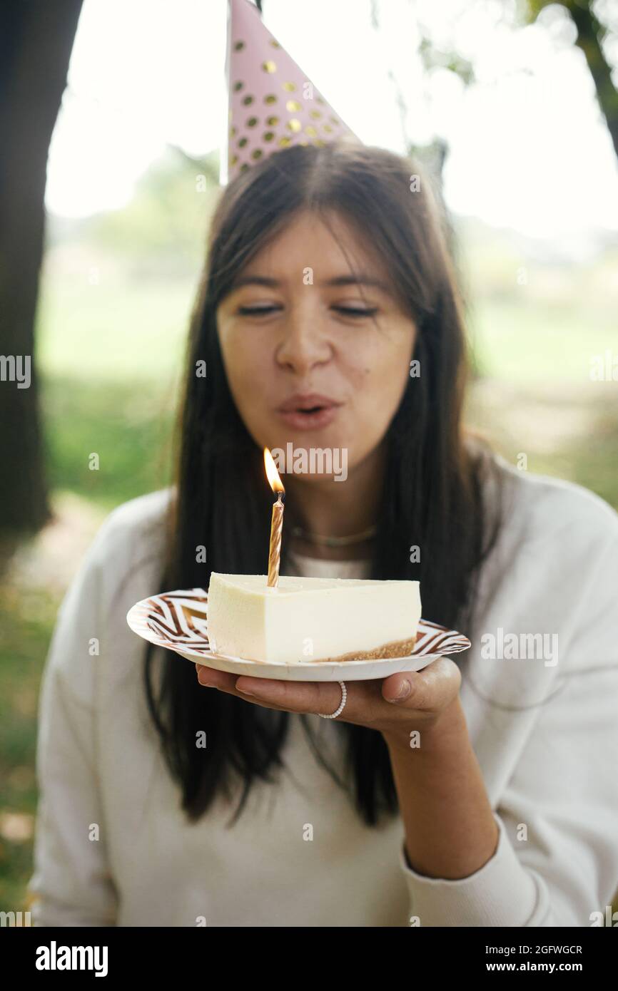 Elegante Femme Heureuse Dans Un Chapeau De Fete Tenant Un Morceau De Gateau D Anniversaire Avec Bougie En Feu Et De Faire Un Souhait Fete D Anniversaire A L Exterieur Photo Stock Alamy