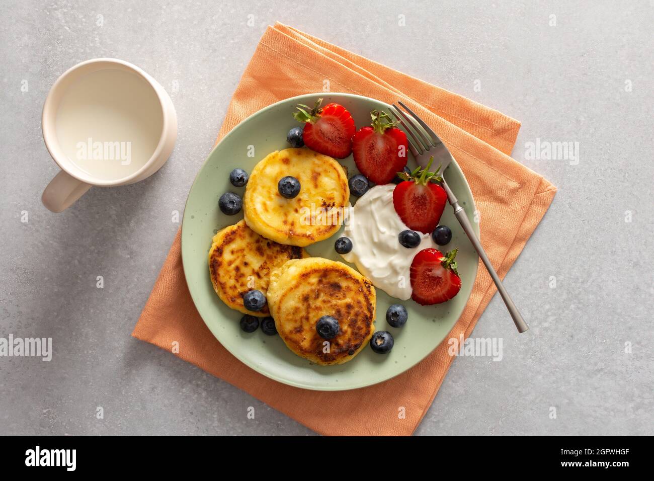 Crêpes au fromage cottage avec fraises, bleuets et crème sure, tasse avec lait, délicieux petit déjeuner, vue sur le dessus Banque D'Images