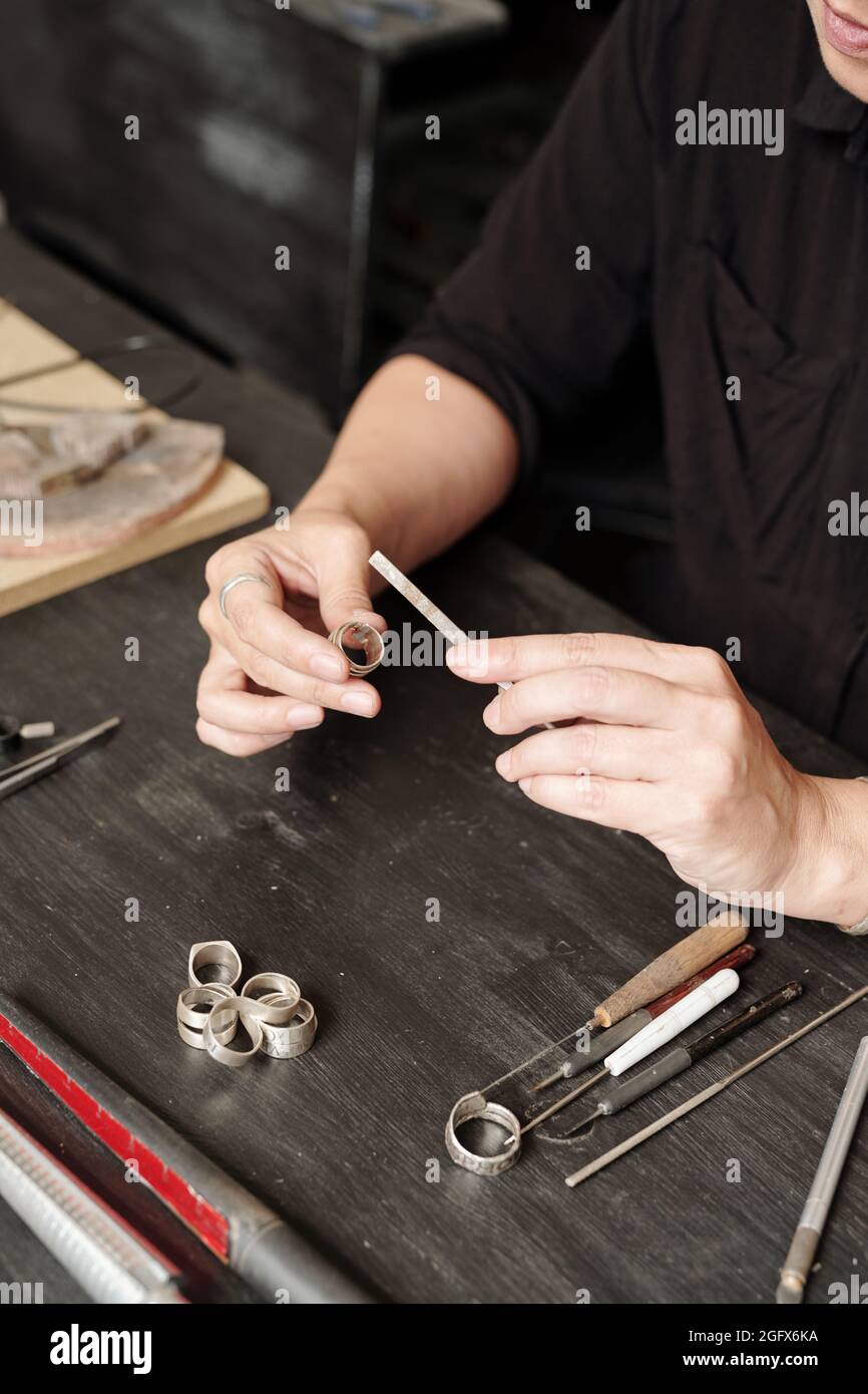 Gros plan d'un bijoutier féminin méconnu assis à la table et d'une bague de polissage avec outil de classement Banque D'Images Gros plan d'un bijoutier féminin méconnu assis à la table et d'une bague de polissage avec outil de classement Banque D'Images