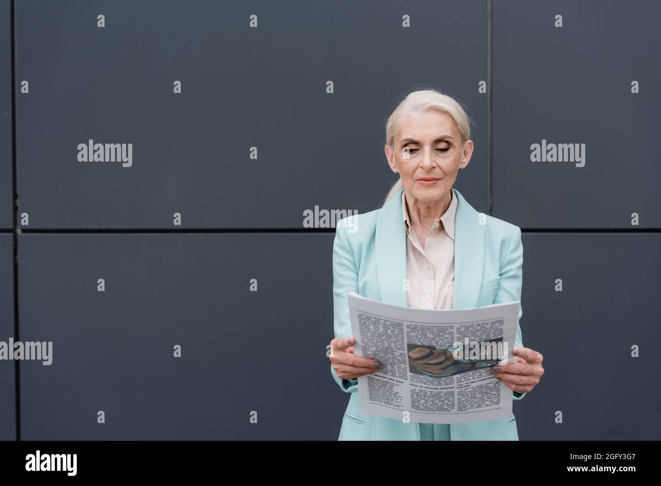 Femme d'affaires senior lisant le journal près d'un bâtiment à l'extérieur Banque D'Images