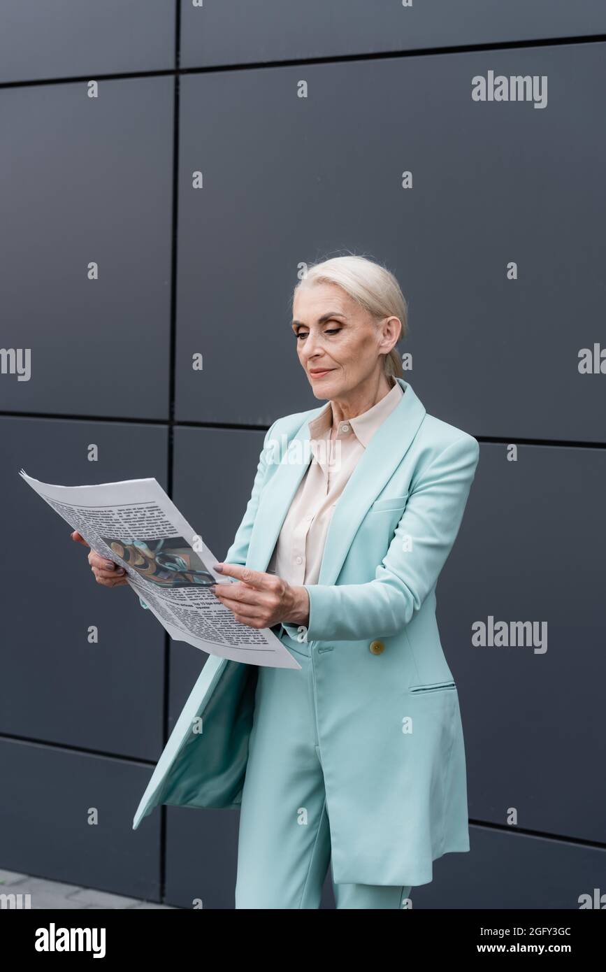 Femme d'affaires âgée lisant des nouvelles près d'un bâtiment à l'extérieur Banque D'Images
