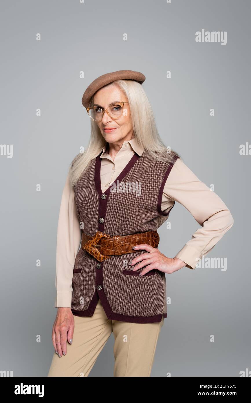 Femme âgée élégante tenant la main sur la hanche isolée sur le gris Banque D'Images