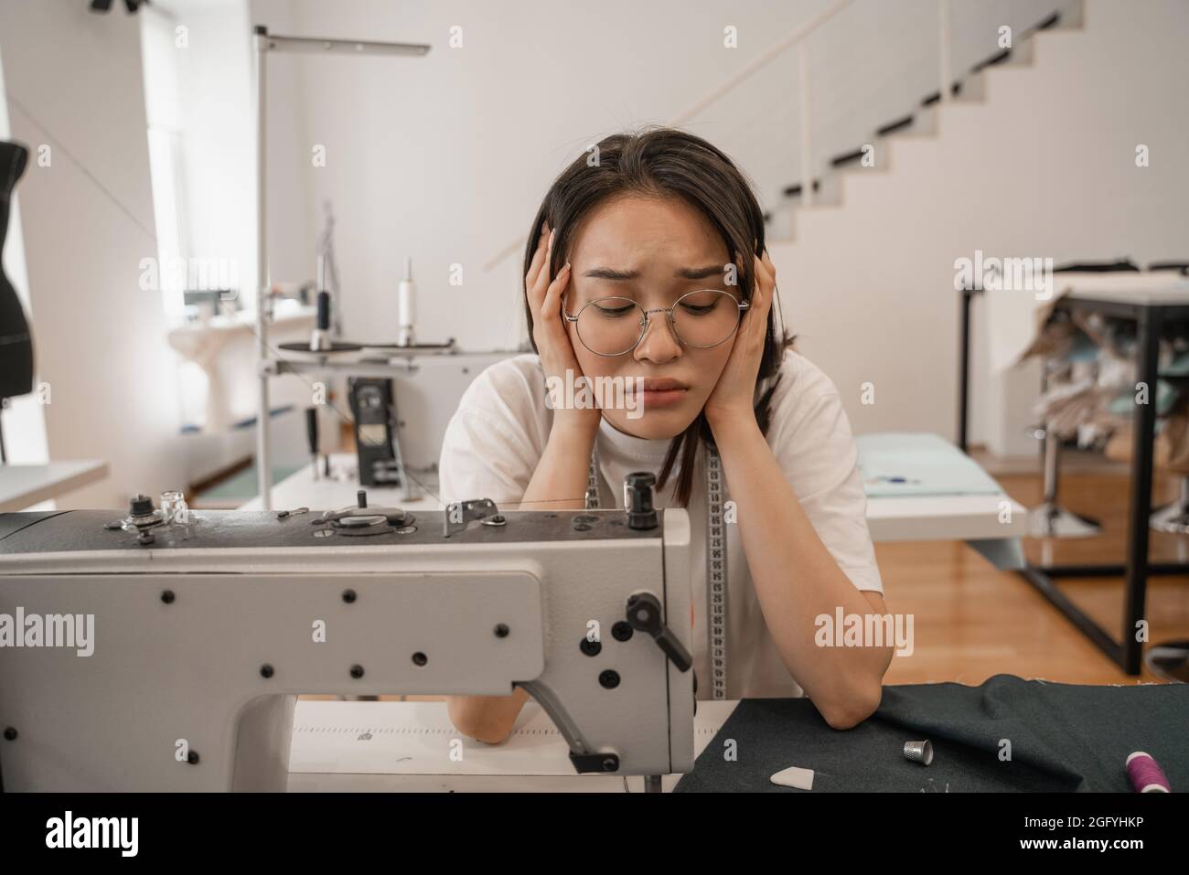 Couturière asiatique fatiguée regardant la machine à coudre et le tissu Banque D'Images