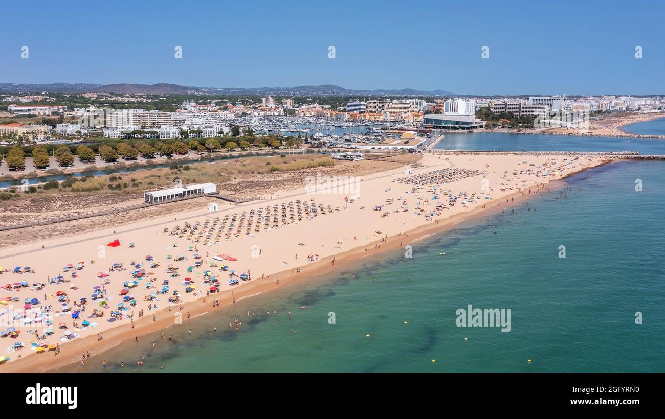 Vue aérienne de la plage de luxe de Falesia à Vilamoura. Avec des touristes bains de soleil sur les chaises longues. Port de plaisance avec yachts, en arrière-plan. Banque D'Images
