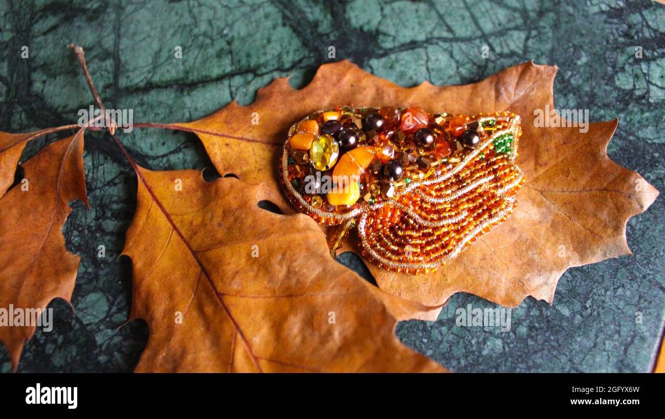La broche pour femmes, sous la forme d'une feuille d'automne, repose sur des feuilles de chêne jaune séchées. Décoration vintage en automne. Banque D'Images