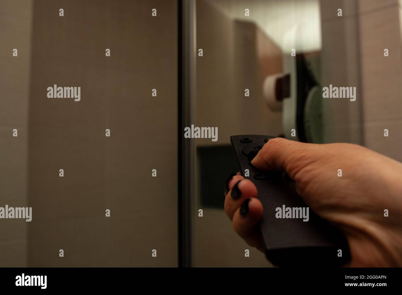 La main de femme appuyant sur le bouton de la télécommande pour donner des ordres de nettoyage automatique nettoie le verre et l'écran de douche Banque D'Images