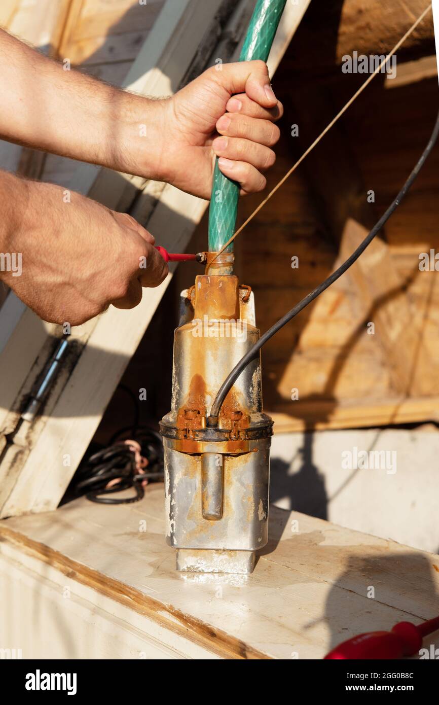 Les mains mâles connectent une pompe de puits avec un flexible à l'aide  d'un collier de serrage et serrez la vis à l'aide d'un tournevis Photo  Stock - Alamy