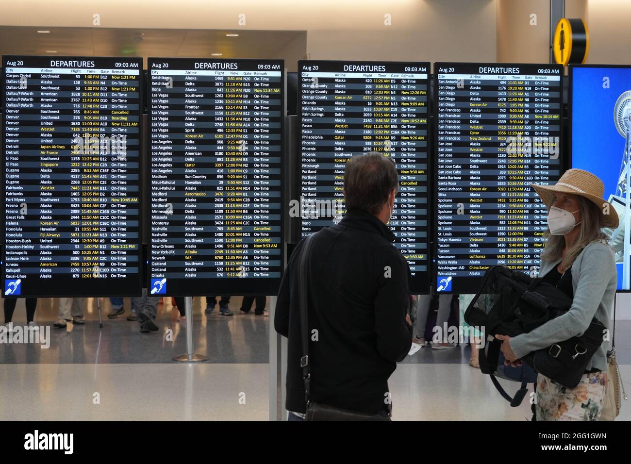 Les personnes avec des masques de visage marchent à côté du panneau des départs au terminal nord de l'aéroport international de Seattle-Tacoma, le vendredi 20 août 2021, in Banque D'Images