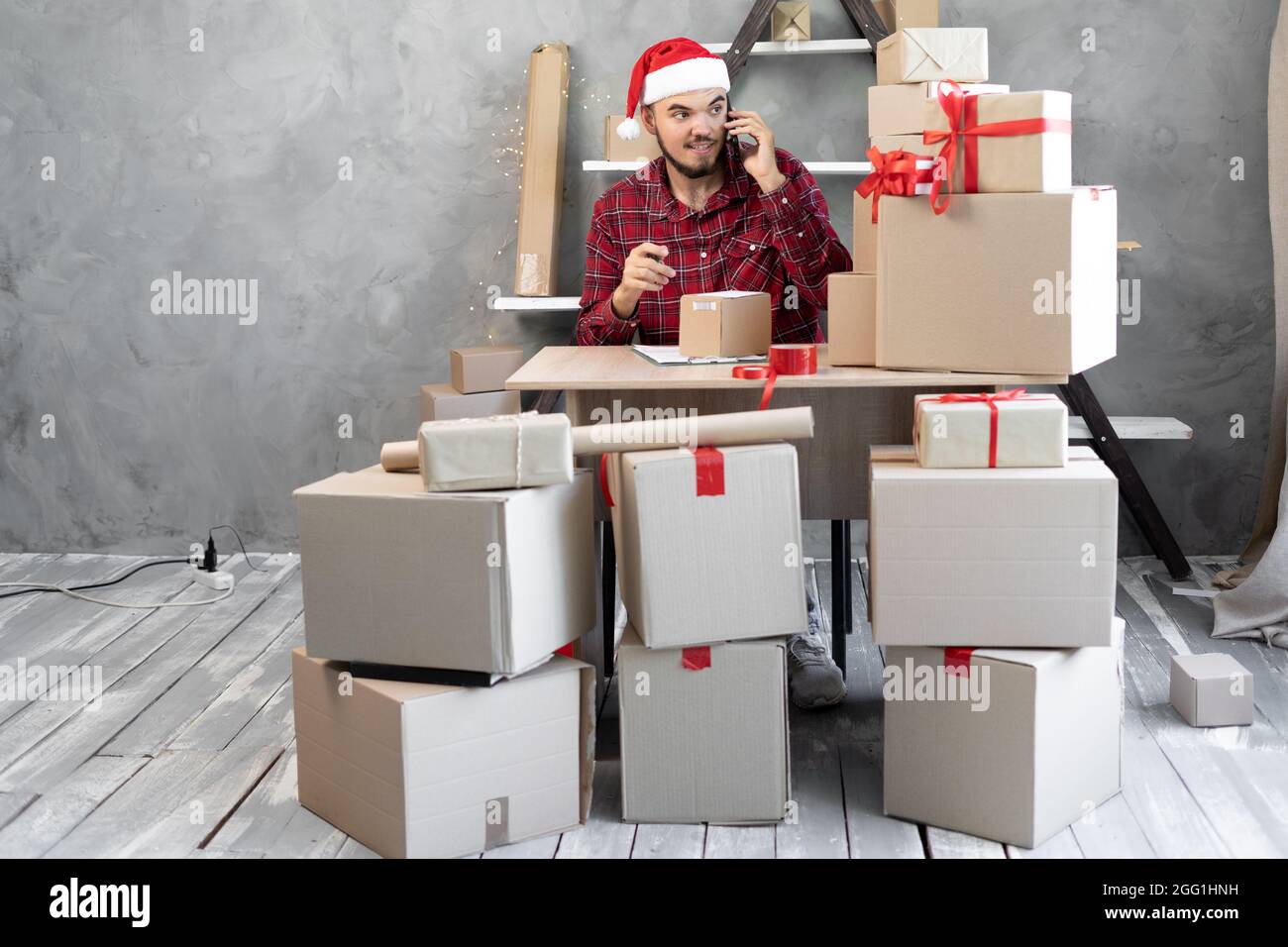 Un jeune père Noël travaille dans un entrepôt, reçoit un appel, commande un produit et écrit un colis pour expédition ou livraison. Nouvel an et Christma Banque D'Images
