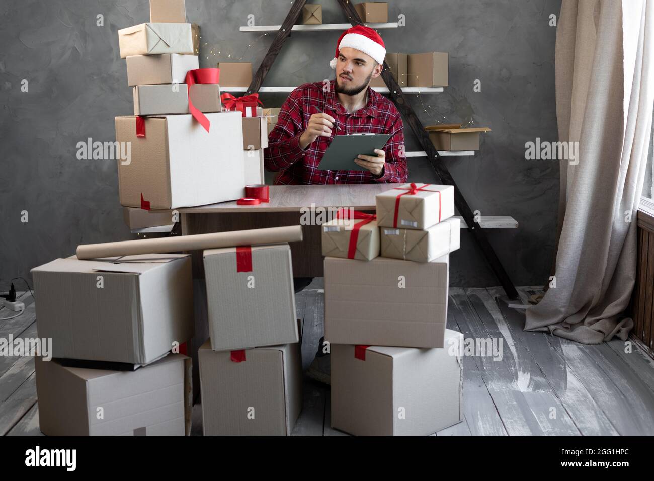 Un homme dans un chapeau de Père Noël travaille à la maison dans un entrepôt avec des boîtes de marchandises ou de cadeaux pour les enfants pour Noël. Comptabilité de marchandises magasin en ligne petit bus Banque D'Images