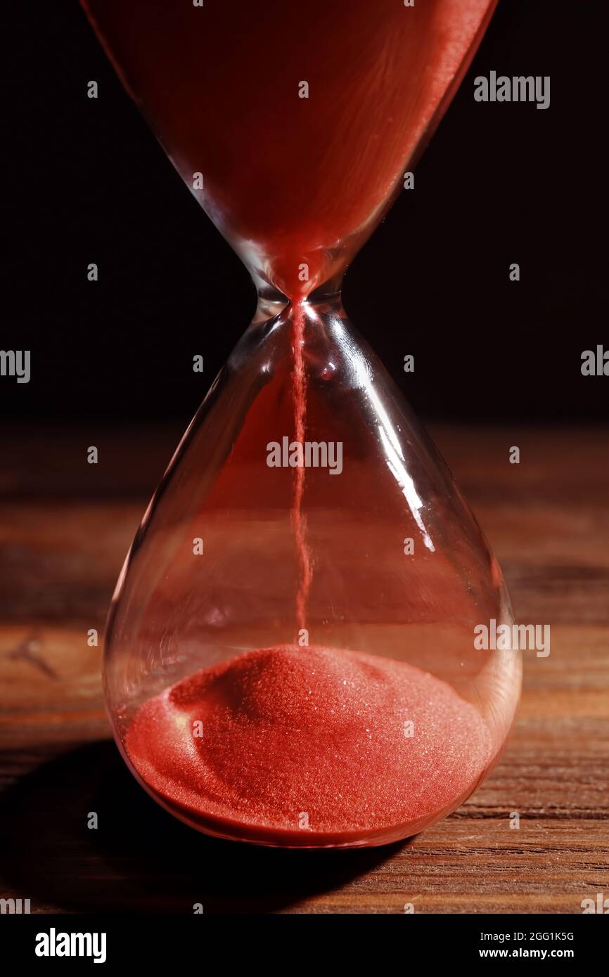 Concept Le temps qui passe. Sablier de cristal avec du sable rouge sur fond  sombre et table en bois Photo Stock - Alamy