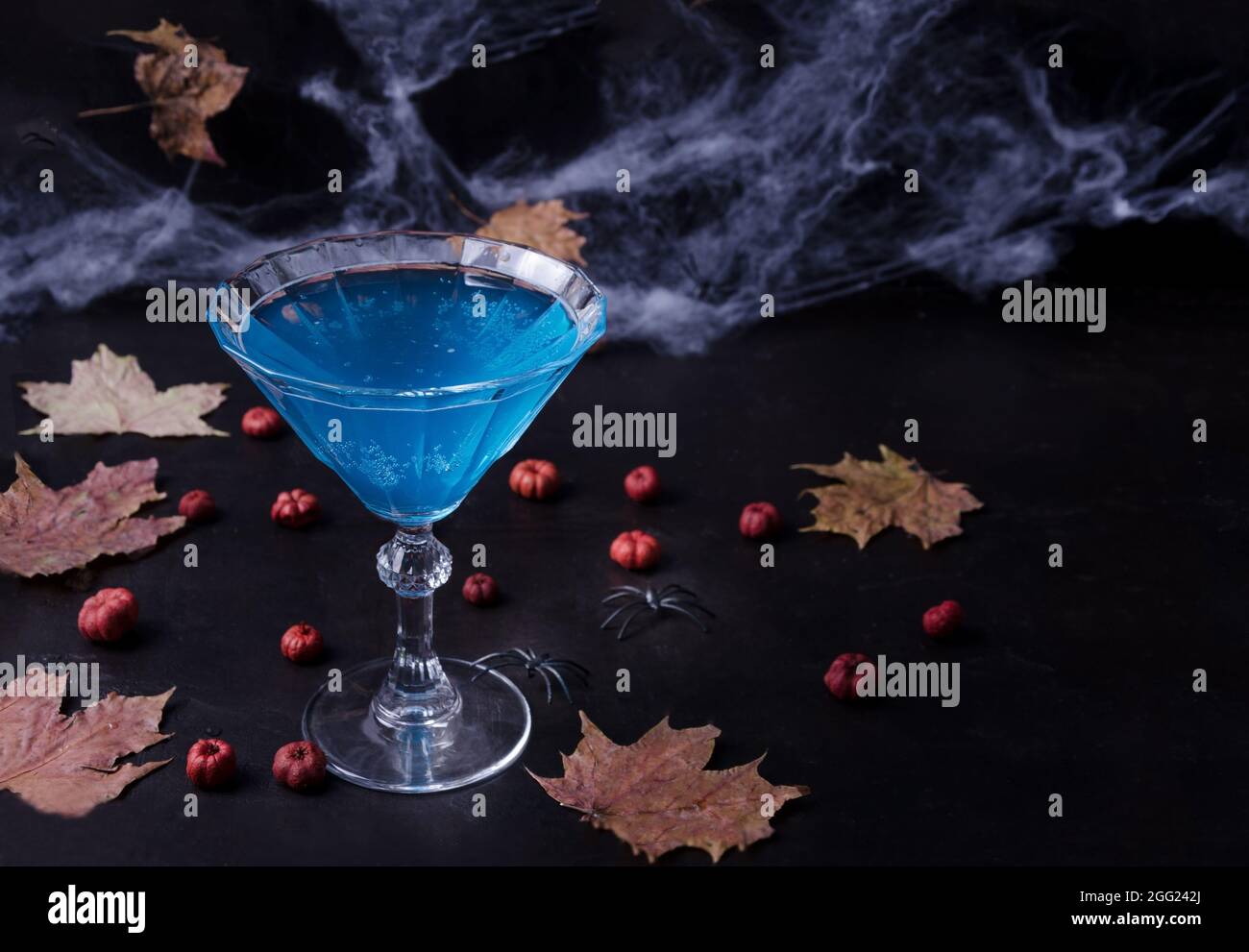 Composition Halloween avec boisson festive, cocktail bleu et mini citrouilles, toile d'araignée et feuilles mortes sur fond noir, mise au point sélective Banque D'Images