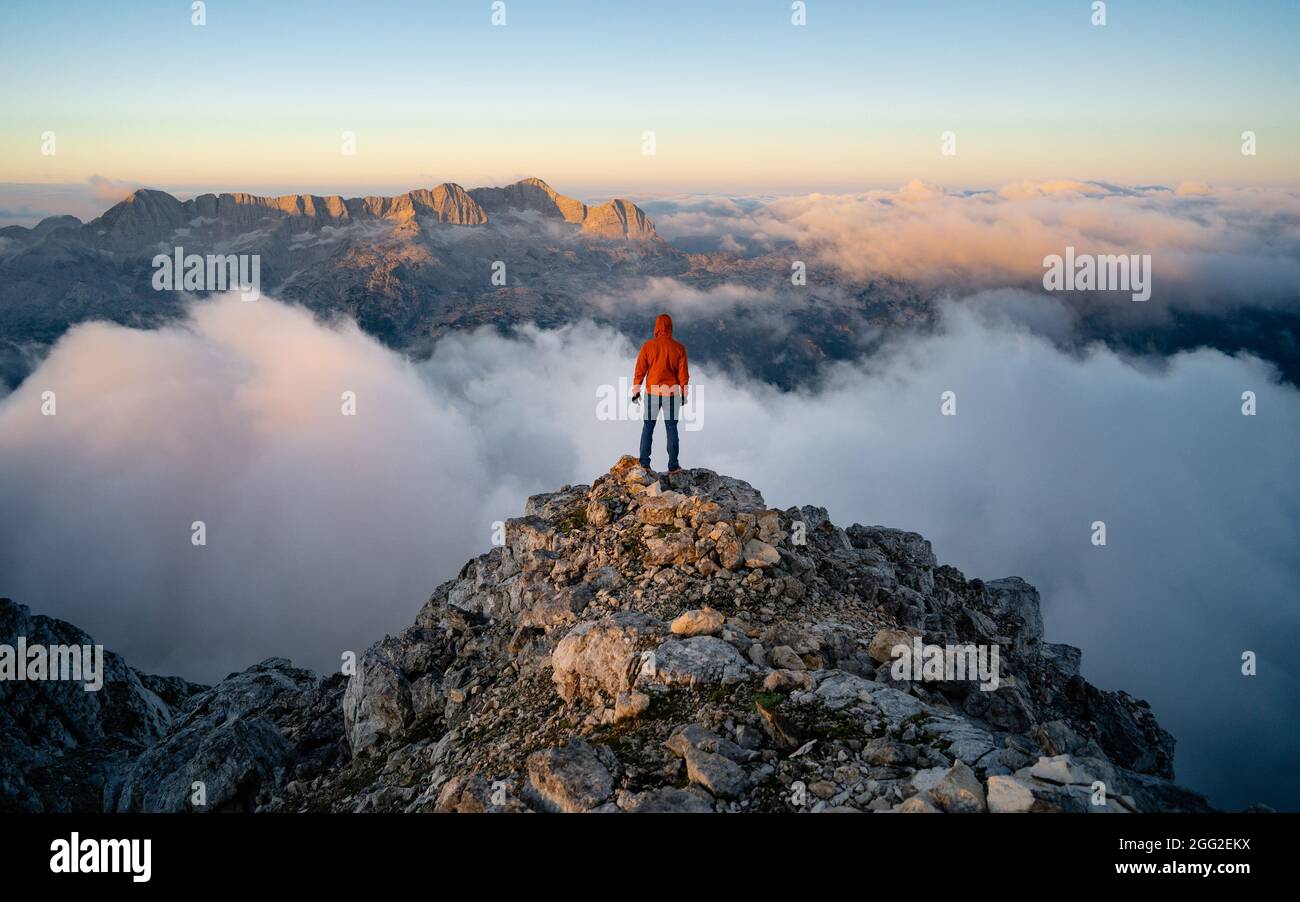 Homme avec sac à dos haut au-dessus de la vallée de montagne brumeux. La personne seule regarde une montagne entourée de brume et de nuages avec le pic visible. SC Banque D'Images