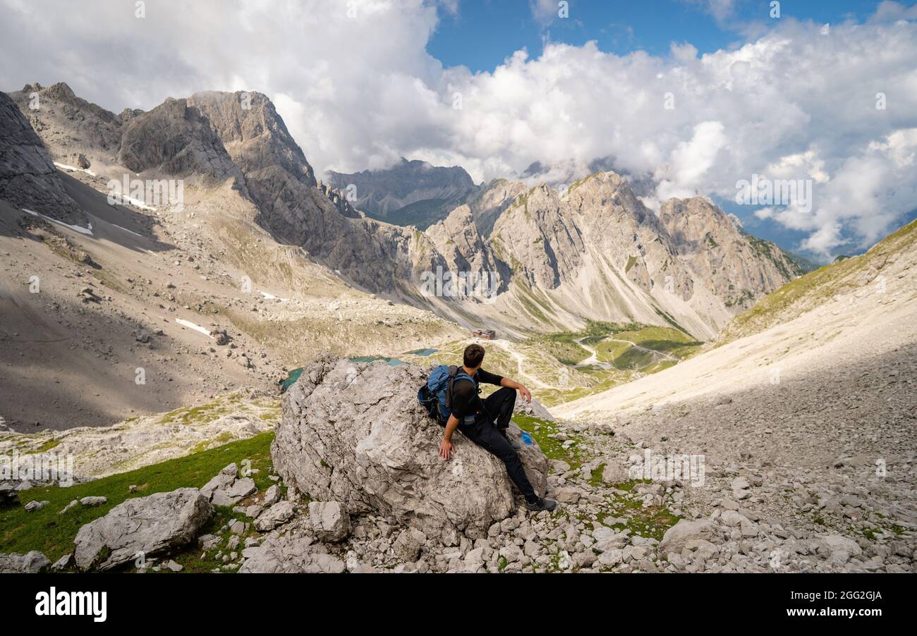 Jeune homme en vêtements de sport et assis sur des rochers en admirant le paysage de montagne de pierreux de Lienz Dolomites, Autriche. Escalade dangereuse. Banque D'Images
