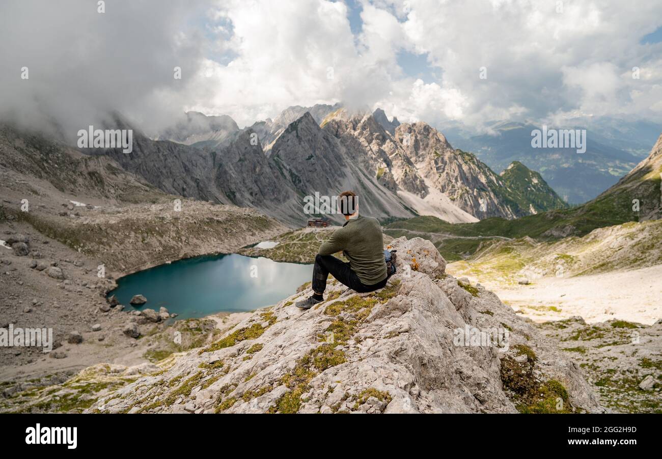 Jeune homme en vêtements de sport et assis sur des rochers en admirant le paysage de montagne de pierreux de Lienz Dolomites, Autriche. Escalade dangereuse. Banque D'Images