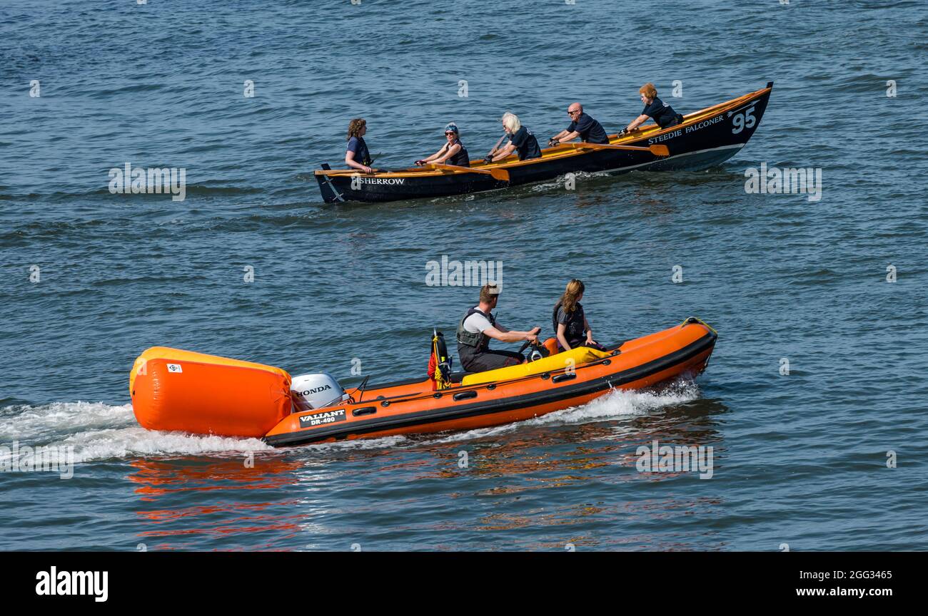 North Berwick, East Lothian, Écosse, Royaume-Uni, 28 août 2021. Météo au Royaume-Uni : sports nautiques. Photo : un bateau de skiff de St Ayle en aviron côtier se prépare dans le Firth de Firth pour une régate avec un bateau gonflable rigide à coque qui passe devant Banque D'Images