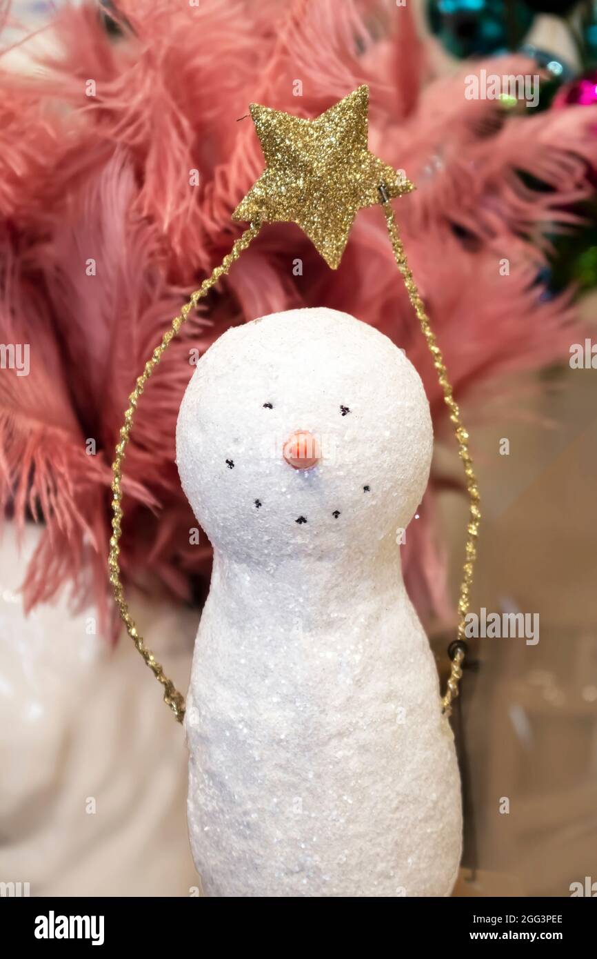 Décoration de bonhomme de neige de Noël étincelante simple tenant une étoile dorée scintillante sur sa tête devant des plumes roses et des boules Banque D'Images