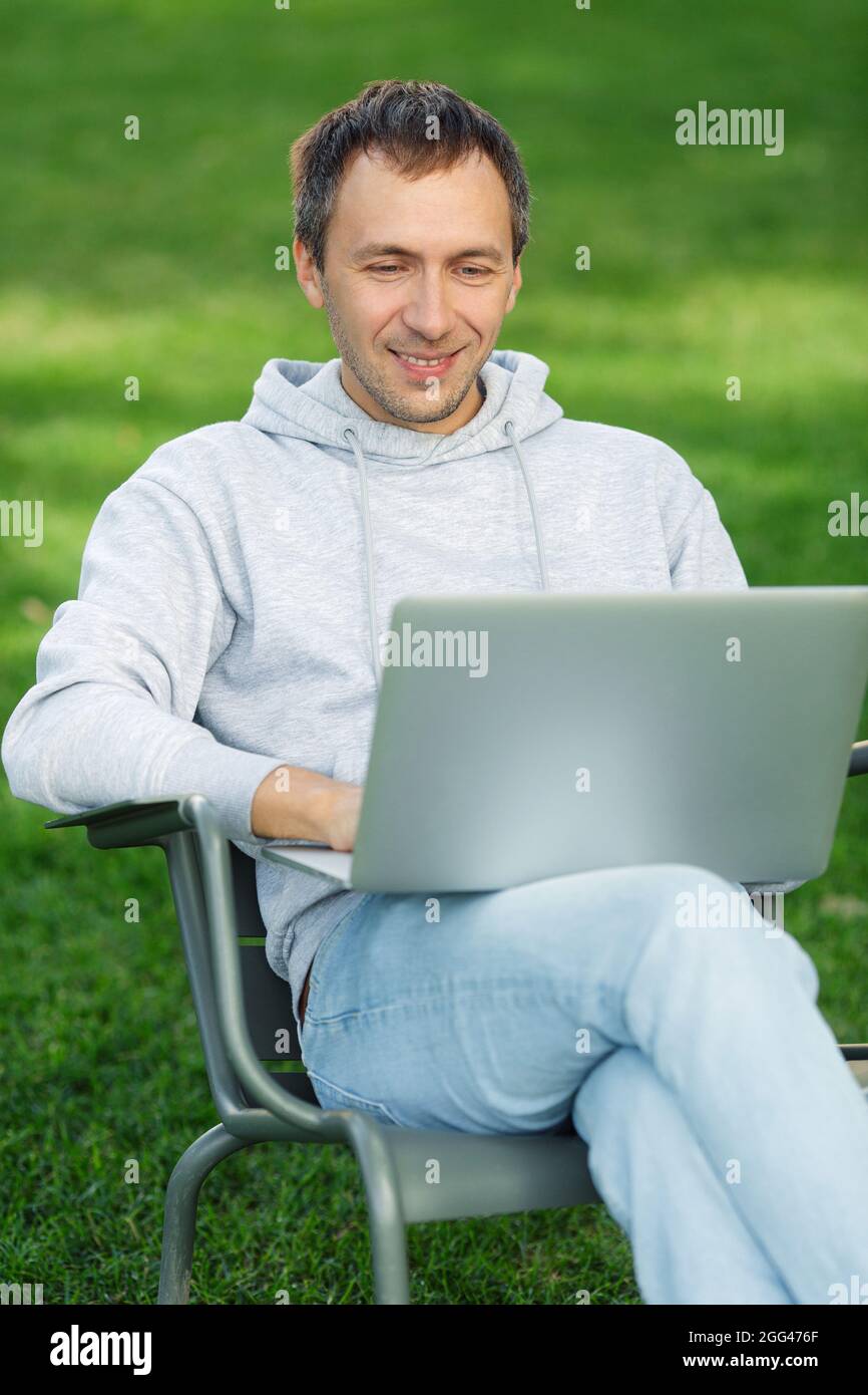 Blogueur homme travaille sur ordinateur portable dans le parc public, traite la vidéo pour le contenu des médias sociaux, assis dans la chaise Banque D'Images