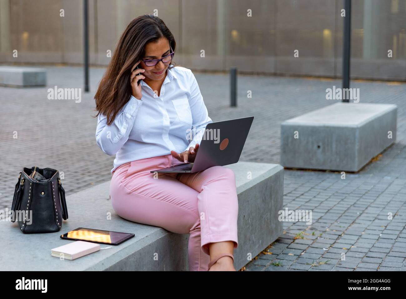 Femme d'affaires caucasienne avec ordinateur portable et téléphone mobile à l'extérieur Banque D'Images