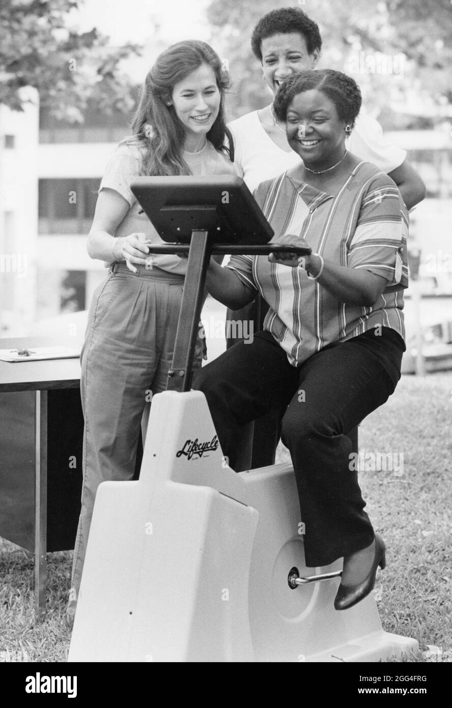 Austin Texas USA, vers 1990: La femme noire vérifie son rythme cardiaque tout en faisant un vélo d'exercice de cycle de vie lors d'une démonstration parrainée par l'hôpital dans un salon de santé dans un parc de la ville. ©Bob Daemmrich Banque D'Images
