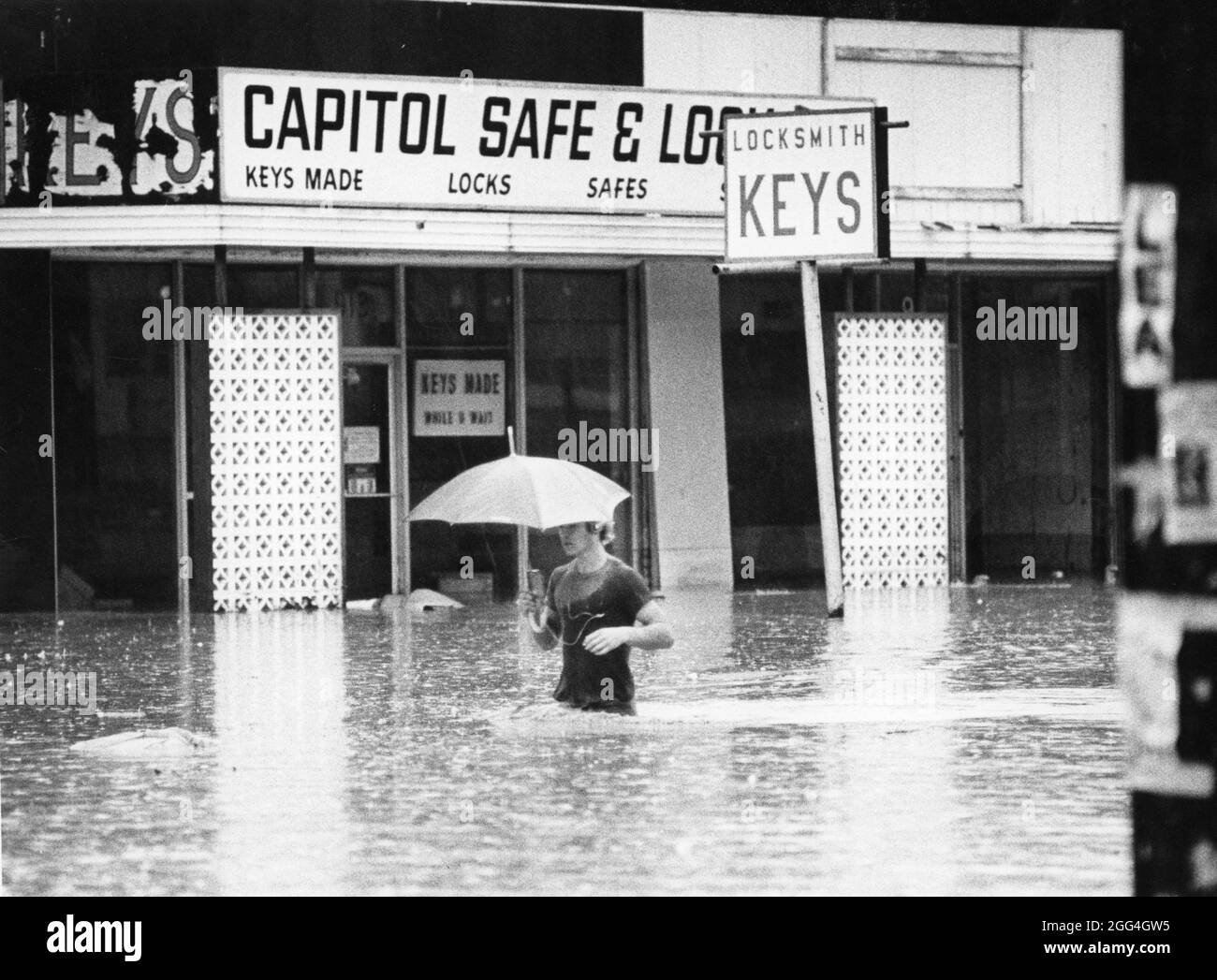 Austin Texas USA, 1982 : un homme tenant un parapluie marche dans l'eau profonde de la hanche devant des entreprises inondées lors d'une crue soudaine sur une rue commerciale. ©Bob Daemmrich Banque D'Images