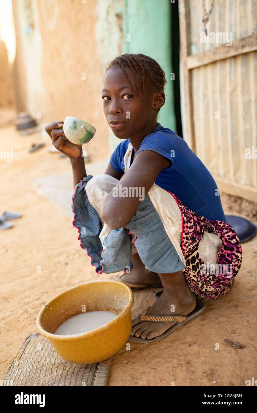 Une jeune fille mange un bol de bouillie de mil pour le petit déjeuner devant la maison de son village dans la région de Ségou, Mali, Afrique de l'Ouest. Banque D'Images