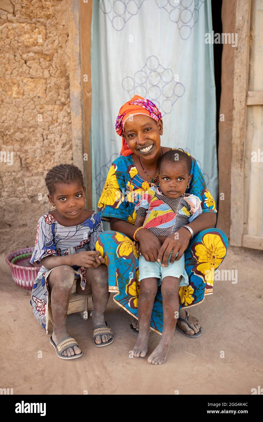 Une jeune mère Fulani et ses deux filles sont assises à l'entrée de leur maison construite dans la boue dans la région de Ségou, Mali, Afrique de l'Ouest. Banque D'Images