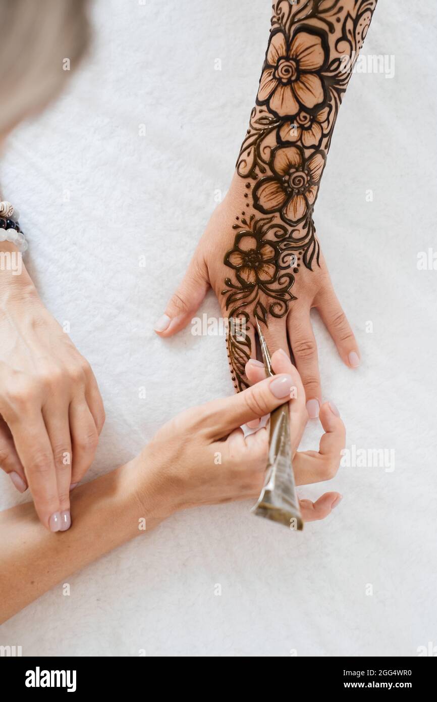 Vue de dessus art henné tatouage sur les mains des femmes. Maître artiste dessin arabe mehndi pour la mariée avant le mariage. Gros plan, vue de dessus. Motif fleuri. Cône Banque D'Images