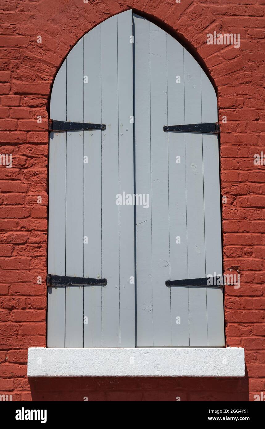 Fenêtre voûtée avec volets en bois fermés sur un mur en brique rouge. Vue sur la rue, photo de voyage, mise au point sélective. Banque D'Images