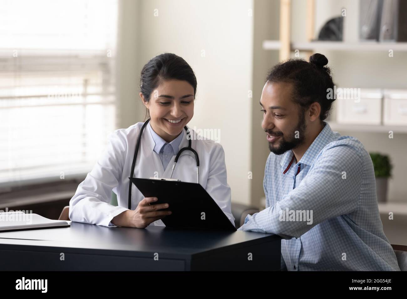 Un jeune médecin indien heureux discutant du traitement avec un patient africain. Banque D'Images