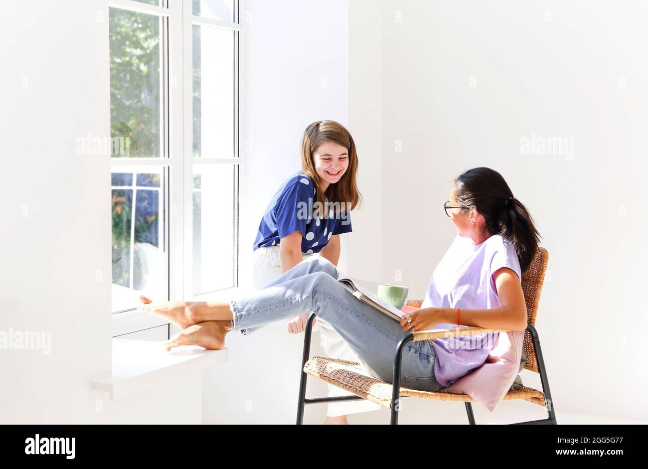 Deux joyeuses femmes décontractées se détendant avec une boisson chaude dans la nouvelle maison. Jeunes filles discutant parler de choses drôles ragots riant dans l'appartement lumineux. Femme Banque D'Images