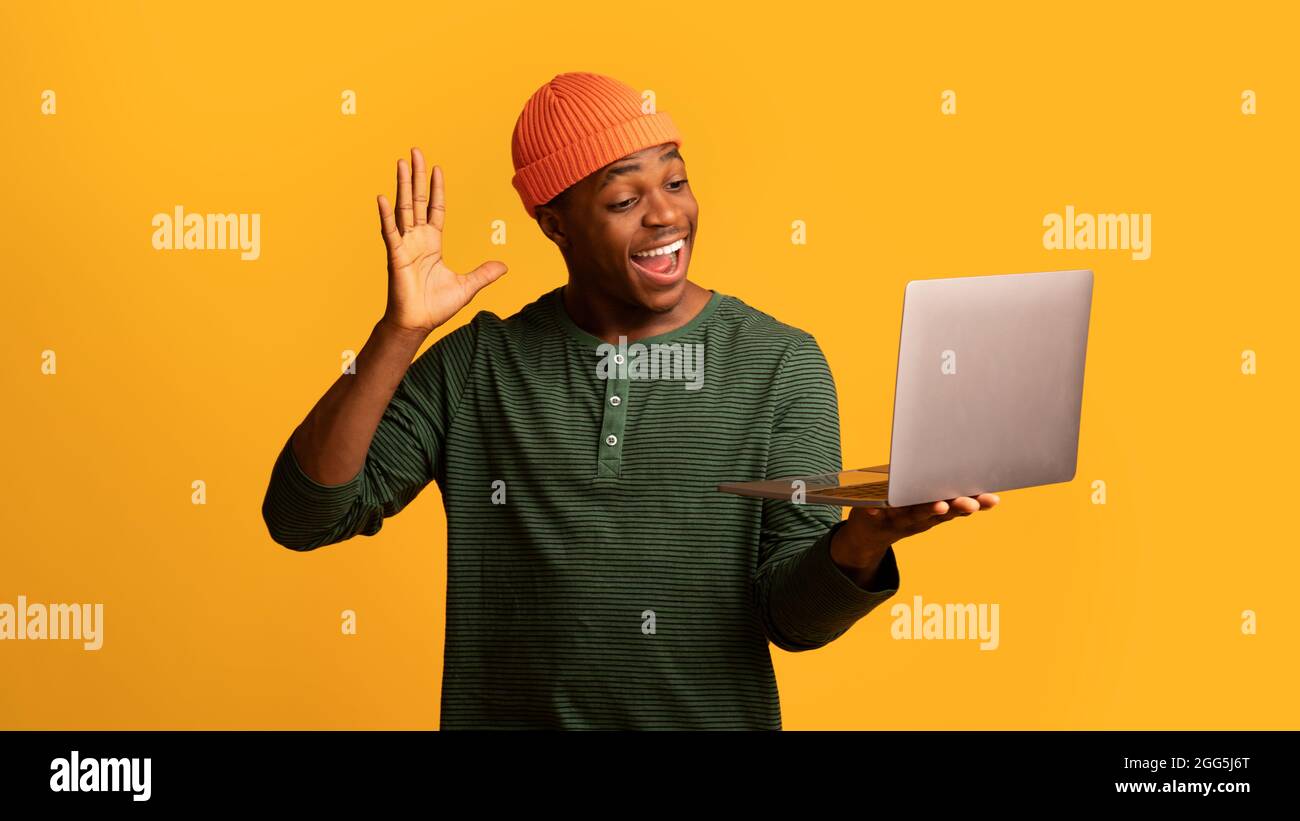 Un homme afro-américain joyeux qui fait des appels vidéo avec un ordinateur portable, en agitant la main à la caméra Banque D'Images