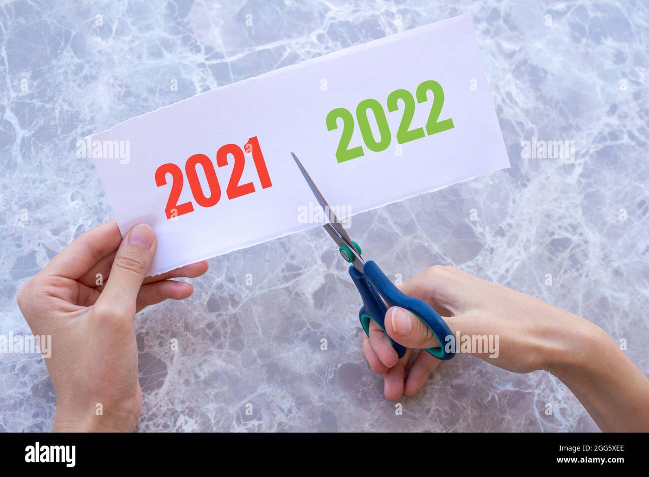La main de la femme coupe le papier avec les mots 2021 et 2022 dessus avec des ciseaux. Concept du nouvel an 2022 à venir. Nouvel an nouveau début. Banque D'Images