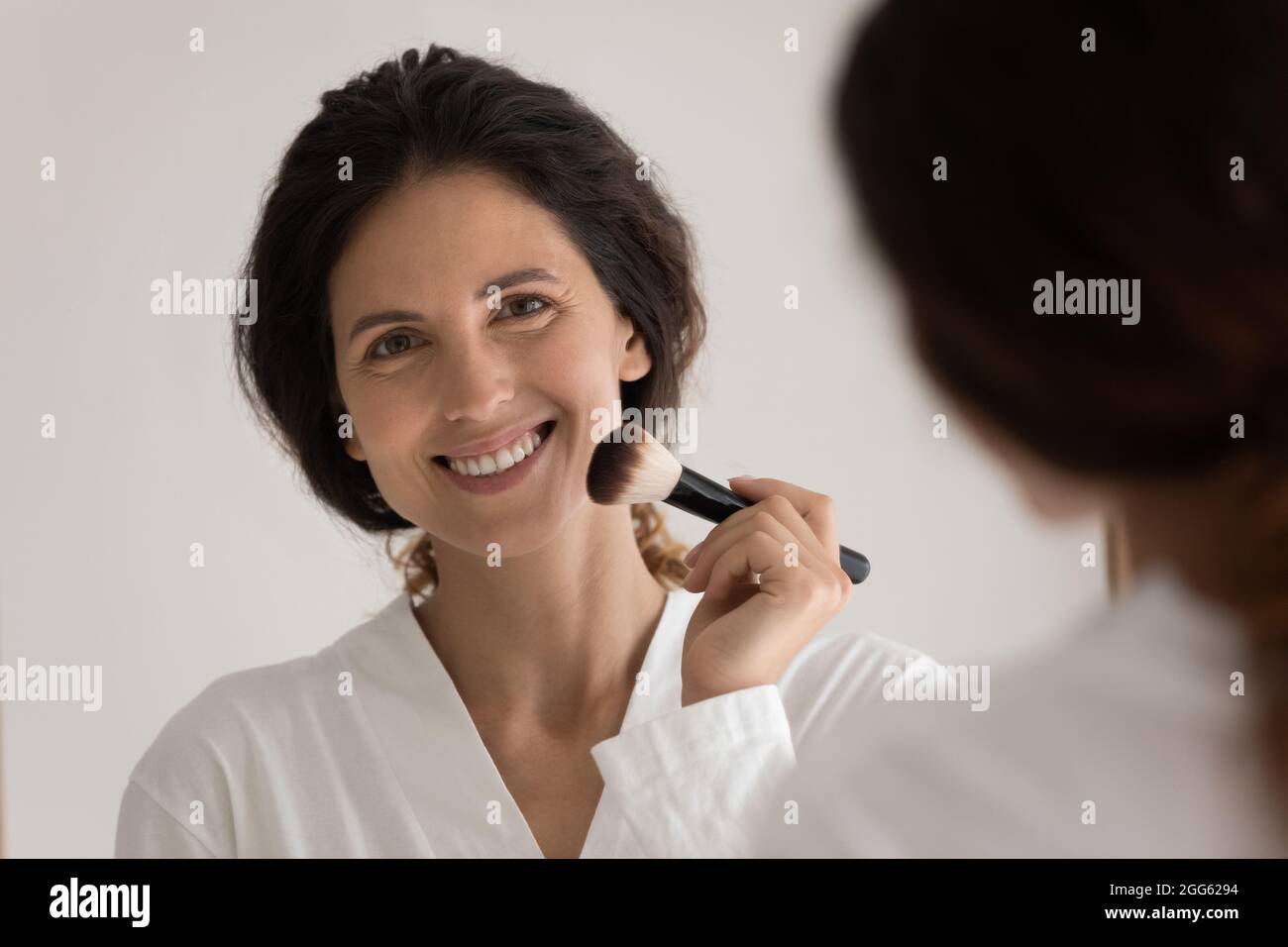 Jeune femme hispanique souriante se maquillant à la maison. Banque D'Images