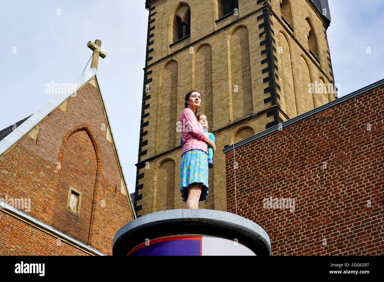 Sculpture réaliste 'Säulenheilige' d'une mère avec son enfant par l'artiste Christoph Pöggeler. Église Saint-Lambertus en arrière-plan. Banque D'Images